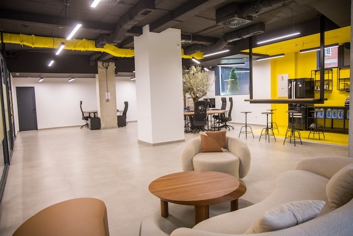 Open coworking workspace at Košnica with desks, monitors, and yellow accent ceiling